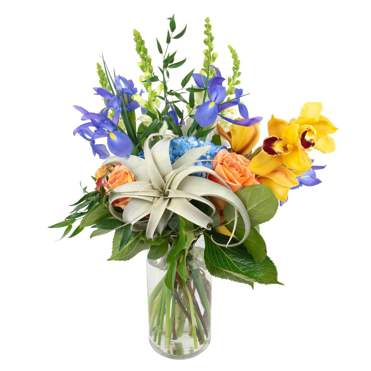Vase with mixed fresh flowers including blue irises, white and yellow orchids, and greenery, arranged in a clear glass vase